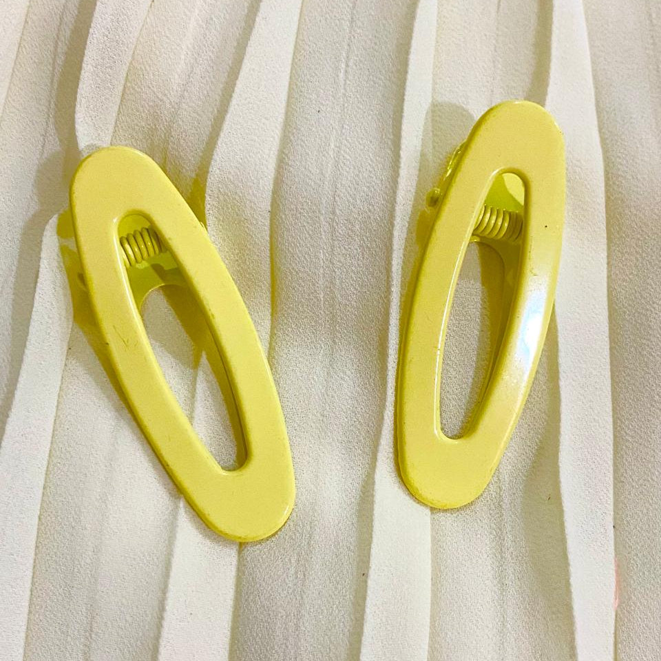 Two yellow hair clips on a white fabric background