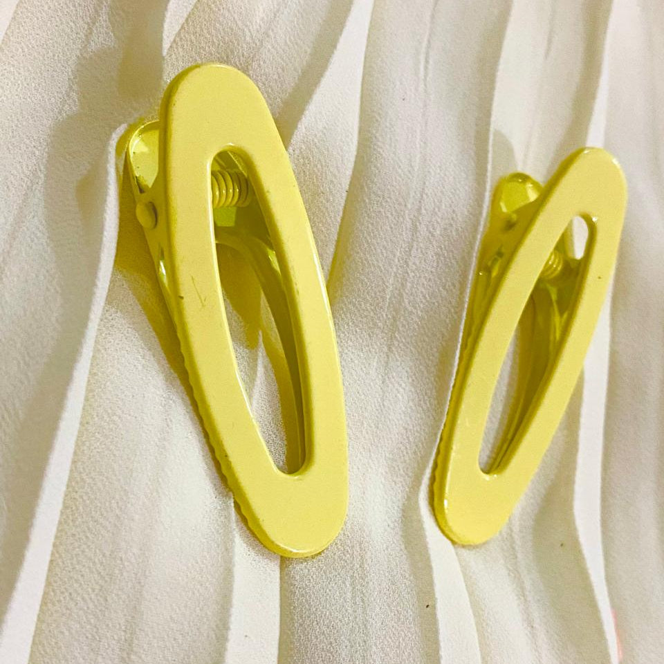 Two yellow hair clips on a white fabric background