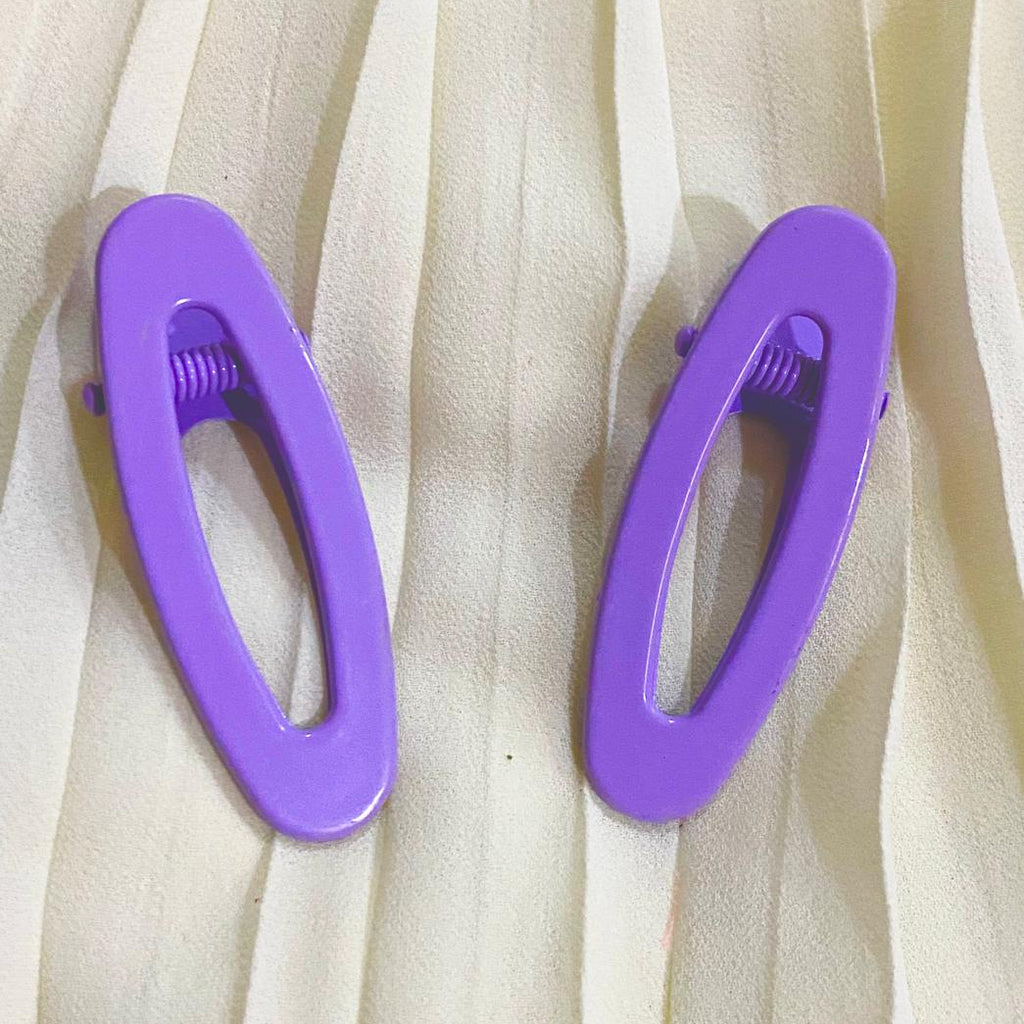 Two purple hair clips on a beige fabric background