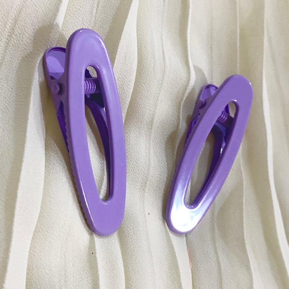 Two purple hair clips on a white fabric background