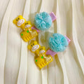Two yellow monkey-shaped hair clips with blue pom-poms on a white curtain background
