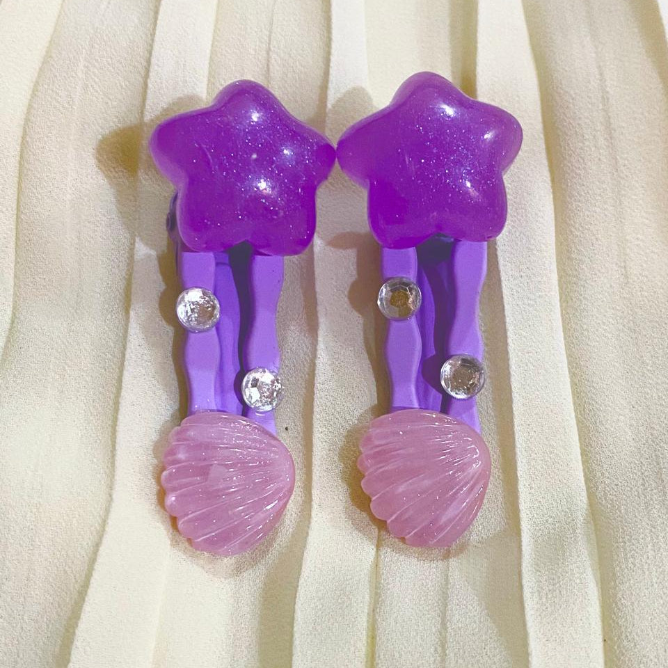 Purple star-shaped hair clips with pink shell designs on a beige fabric background
