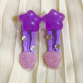 Purple star-shaped hair clips with pink shell designs on a beige fabric background