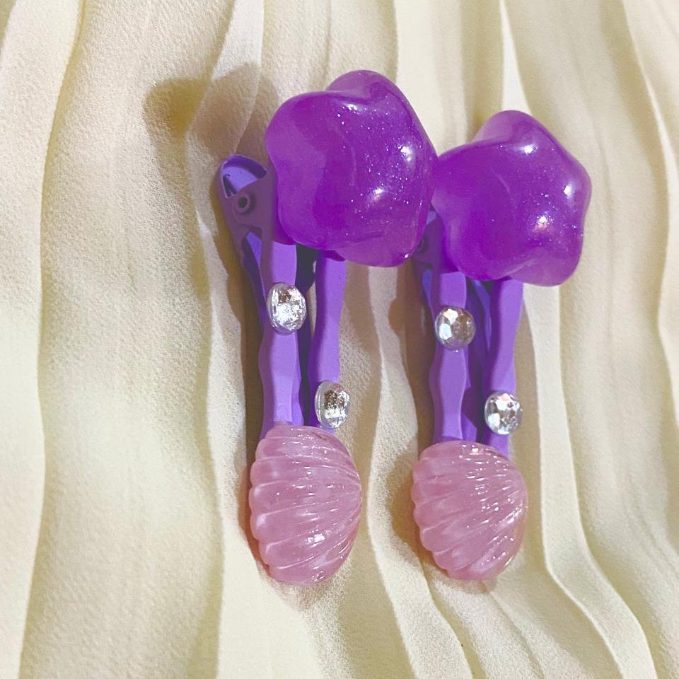 Purple hair clips with pink shells on a beige fabric background