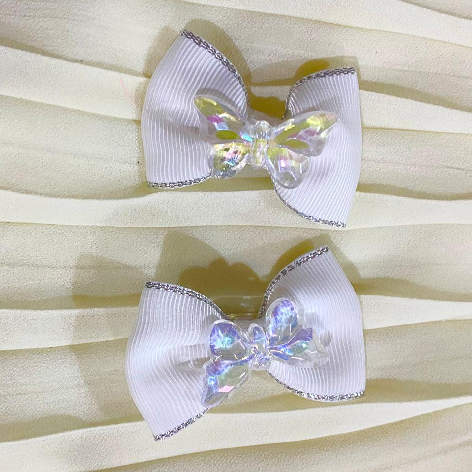 Pair of white bow-shaped earrings with iridescent centers on a beige fabric background dreamy designs