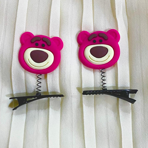 Two pink bear-shaped hair clips with black clips on a white curtain background