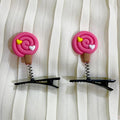 Two pink hair clip designs with black clips on a white curtain background