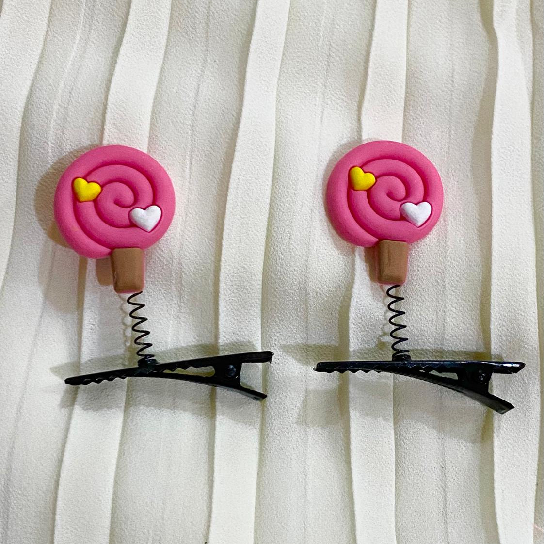 Two pink hair clip designs with black clips on a white curtain background