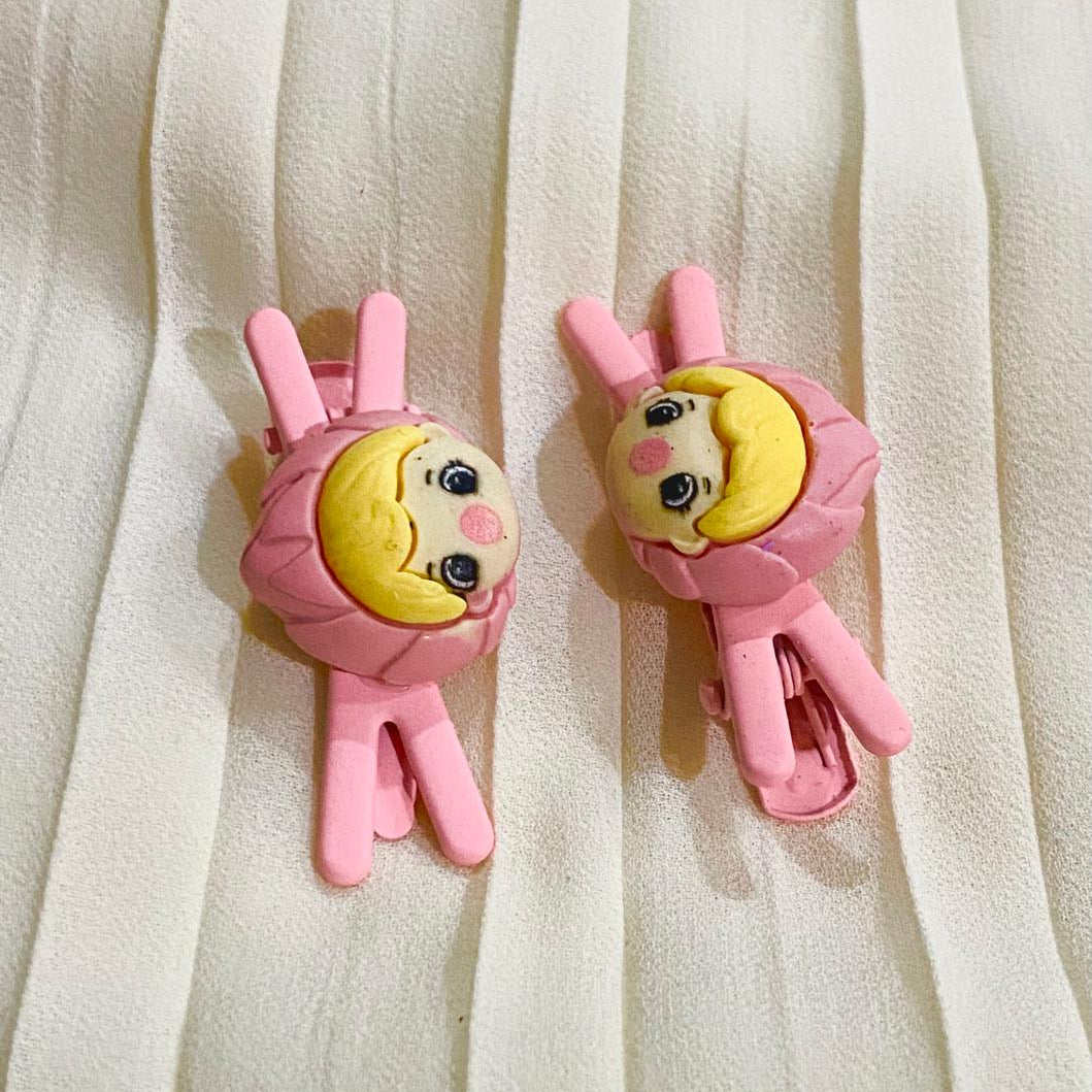 Two pink character hair clips on a white fabric background