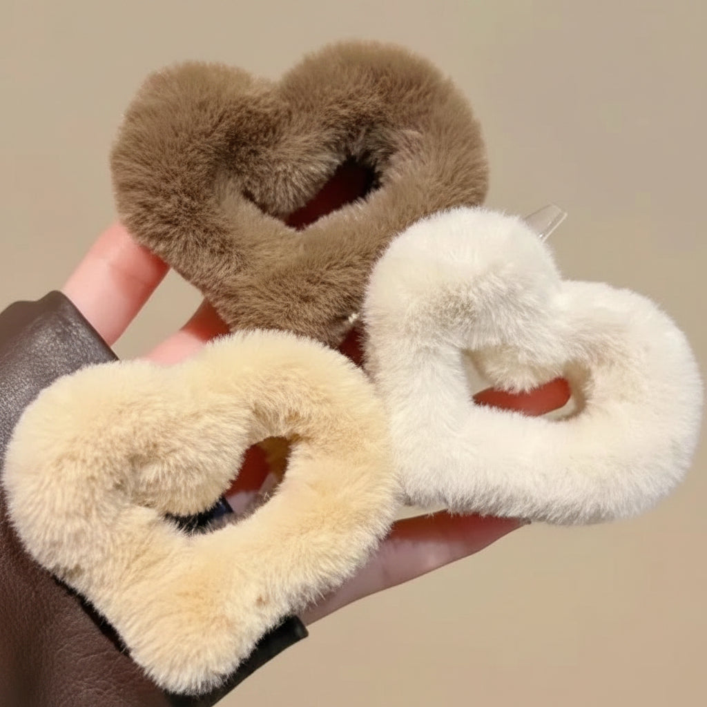 Three heart-shaped hair ties in brown, beige, and white held by a hand against a neutral background.