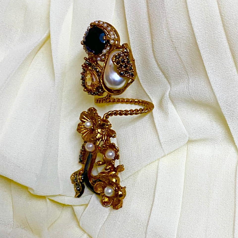 Gold earrings with pearls and a central gemstone on white fabric