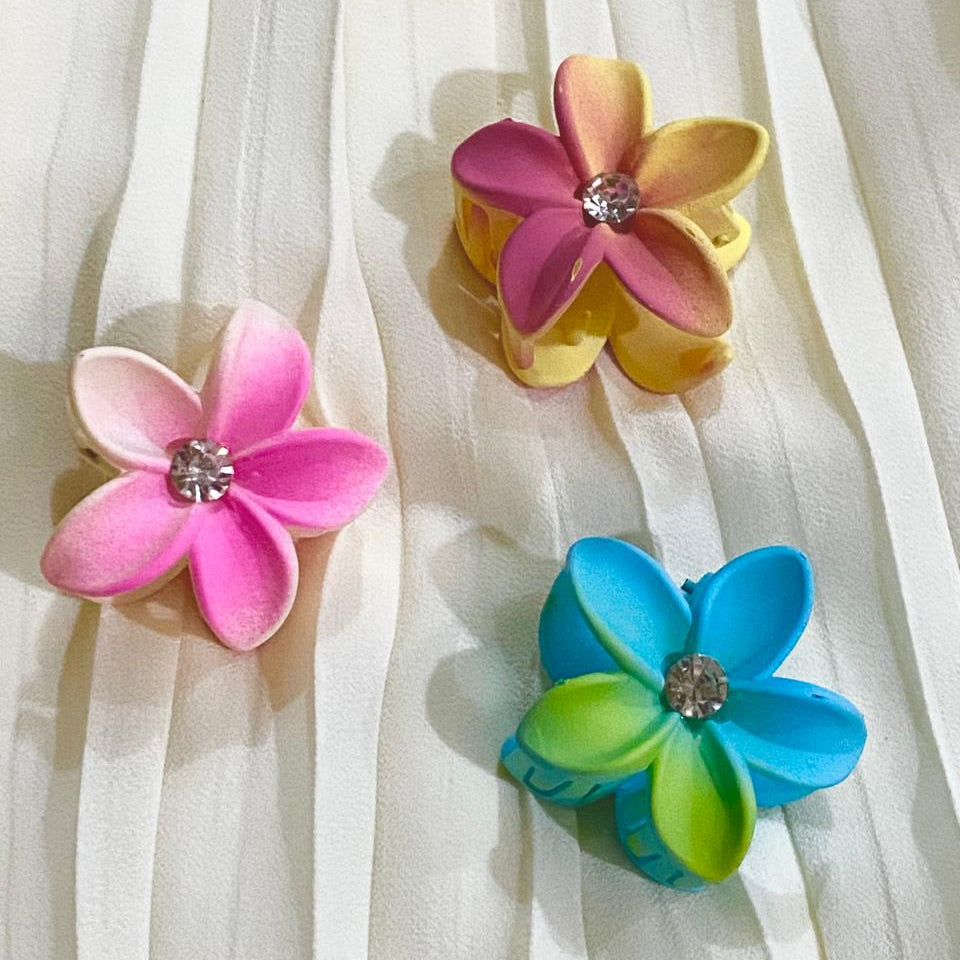Three colorful flower-shaped hair clips on a sheer white curtain background