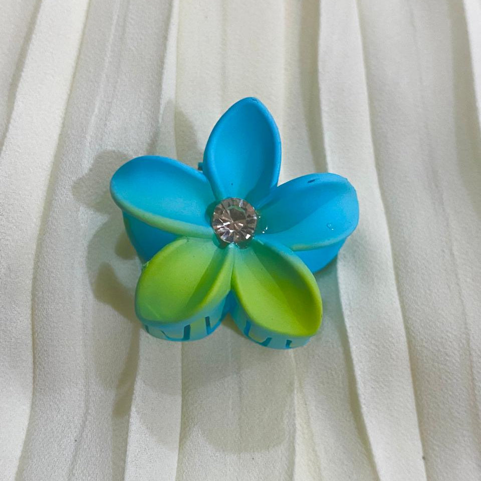 Blue and green flower-shaped hair clip on a white fabric background