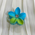Blue and green flower-shaped hair clip on a white fabric background