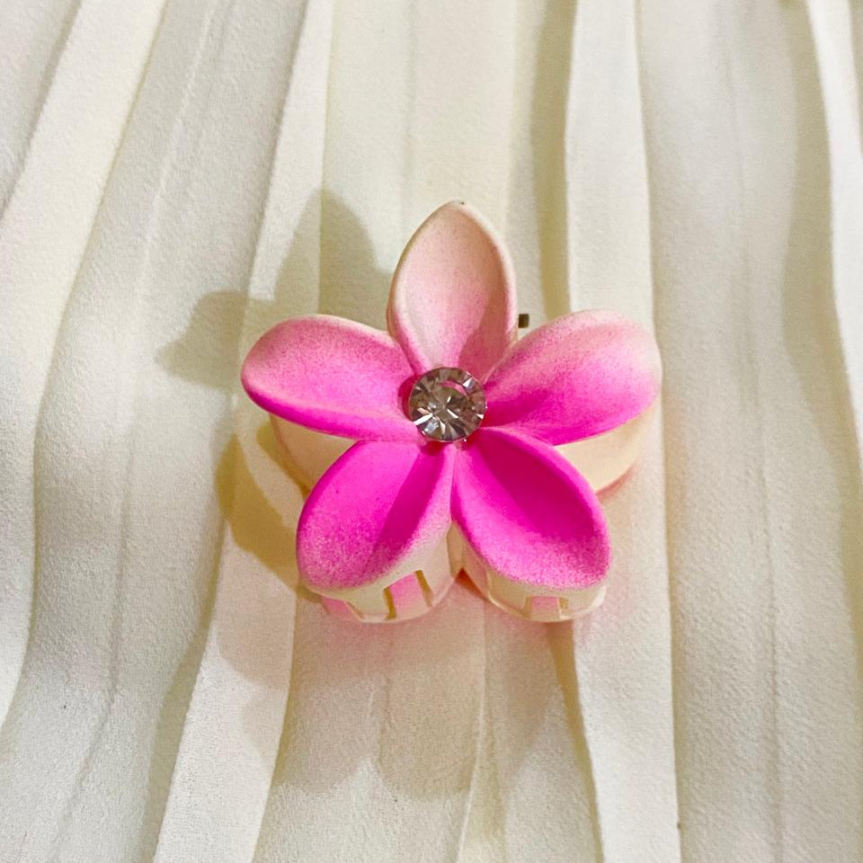 Pink flower-shaped hair clip with a central gemstone on a sheer white fabric background