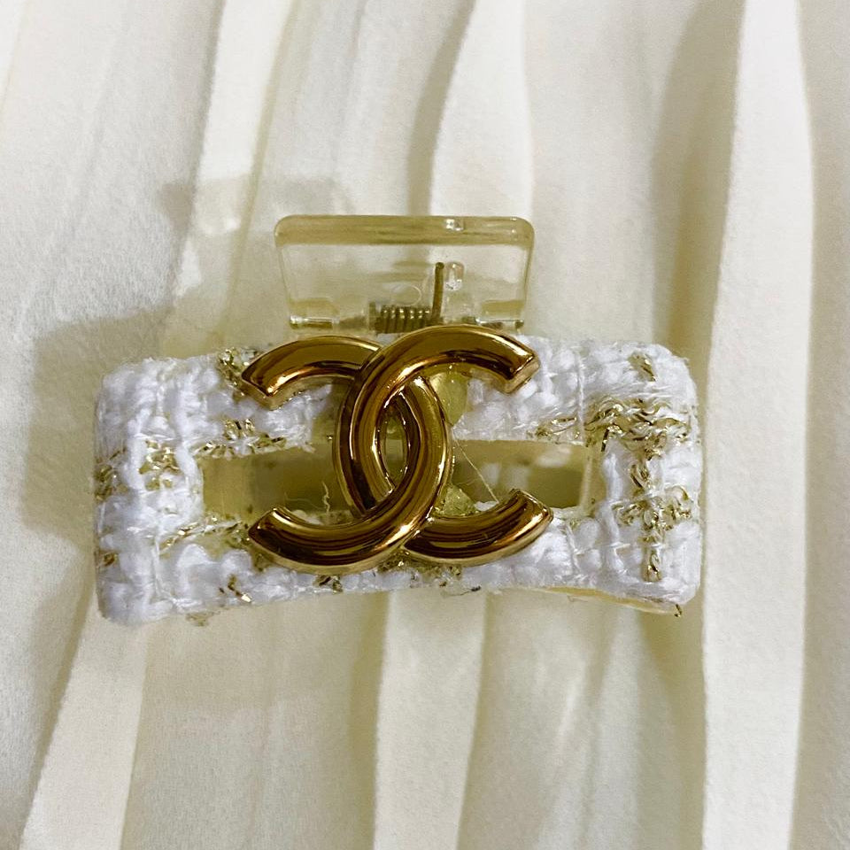 Gold CC logo belt buckle on a white textured belt against a white curtain background