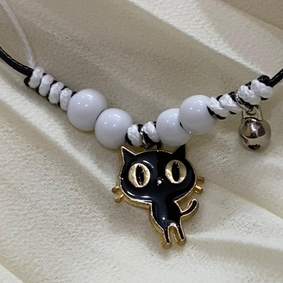 Bracelet with a black cat pendant and white beads on a beige surface