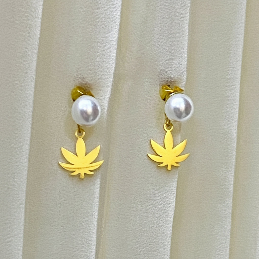 Gold leaf-shaped earrings with white beads on a textured beige background