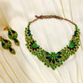 Green and gold necklace and earrings on a white fabric background