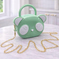 A mint green handbag shaped like a cartoon bear face with white ears and eyes, featuring a gold chain strap, displayed on a light marble table in a bright room.