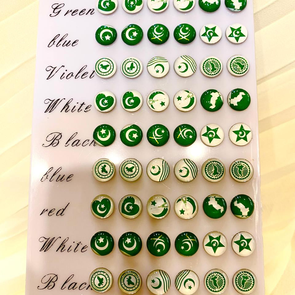 A display card showing multiple rows of round decorative buttons or studs in green, white, black, blue, violet, and plum, each with different crescent and star motifs. The card is photographed on a light beige surface.