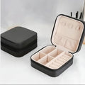 A black zippered jewelry organizer case shown closed on the left and open on the right, with a light beige interior featuring compartments, ring rolls, and ear hooks.