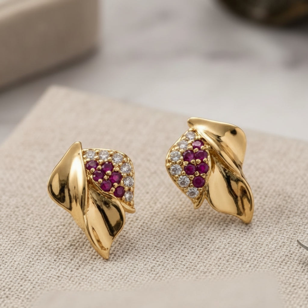 Gold earrings with red gemstones on a light surface