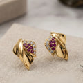 Gold earrings with red gemstones on a light surface
