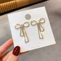 Bow-shaped earrings on a white card held by a hand with red nail polish.