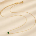 Gold necklace with a green gemstone on a beige background