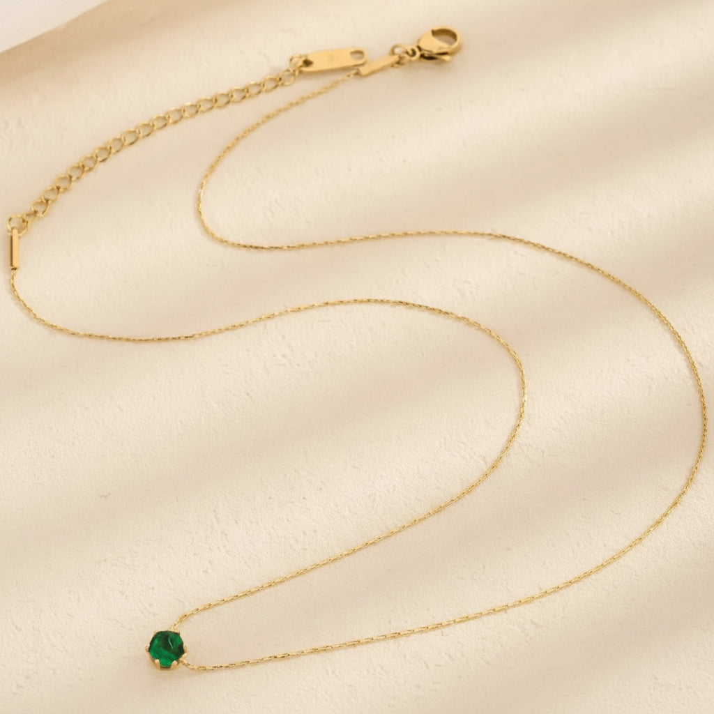 Gold necklace with a green gemstone on a beige background