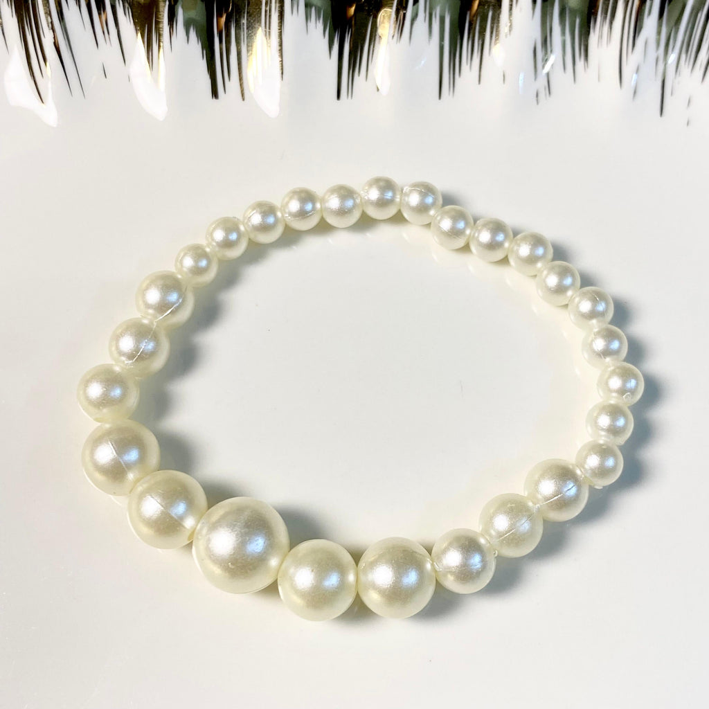 A pearl beaded bracelet arranged in a circle on a white surface, with decorative black and white tinsel at the top edge.
