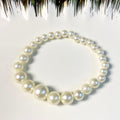 A pearl beaded bracelet arranged in a circle on a white surface, with decorative black and white tinsel at the top edge.