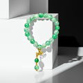 A beaded bracelet made of green marbled and opaque beads with a gold-toned decorative clasp and dangling beads, displayed on a white geometric pedestal.